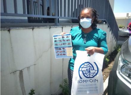 Woman wearing medical mask holds information poster on COVID-19 and IOM donation bag