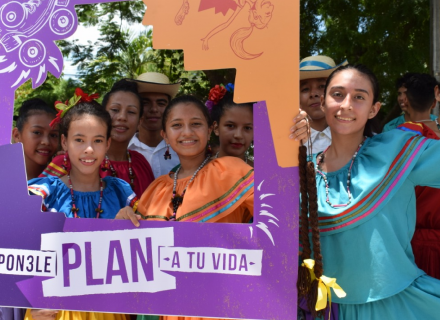 grupo de jóvenes con trajes típicos posan con un marco de fotografías con el logo de la campaña Ponele Plan a tu Vida