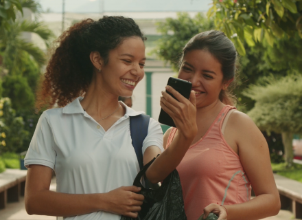 Dos mujeres jóvenes sonríen mientras observan un teléfono celular