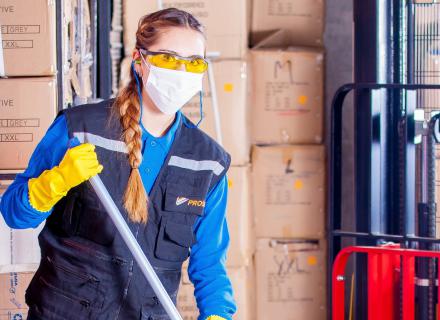 Adult employee wearing personal protection equipment cleans warehouse